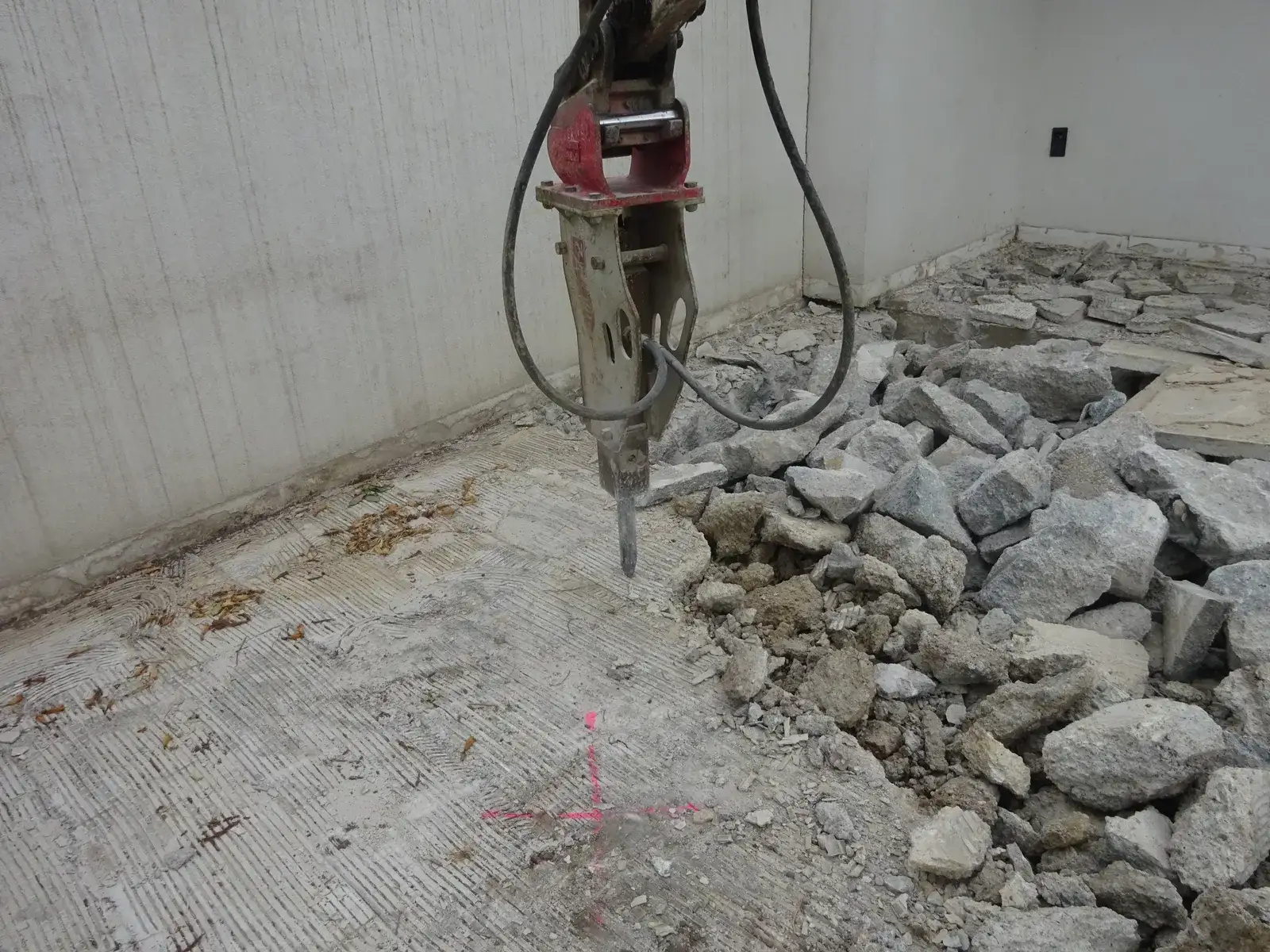 Hydraulikhammer am Bagger bricht einen Betonboden in einem Raum auf, daneben liegen Betonbrocken