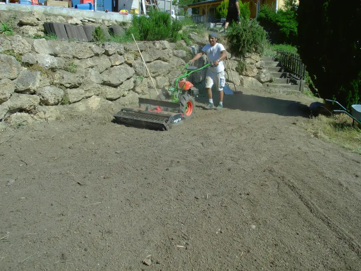 Planierarbeiten im Garten mit der Bodenfräse, dahinter eine Natursteinmauer