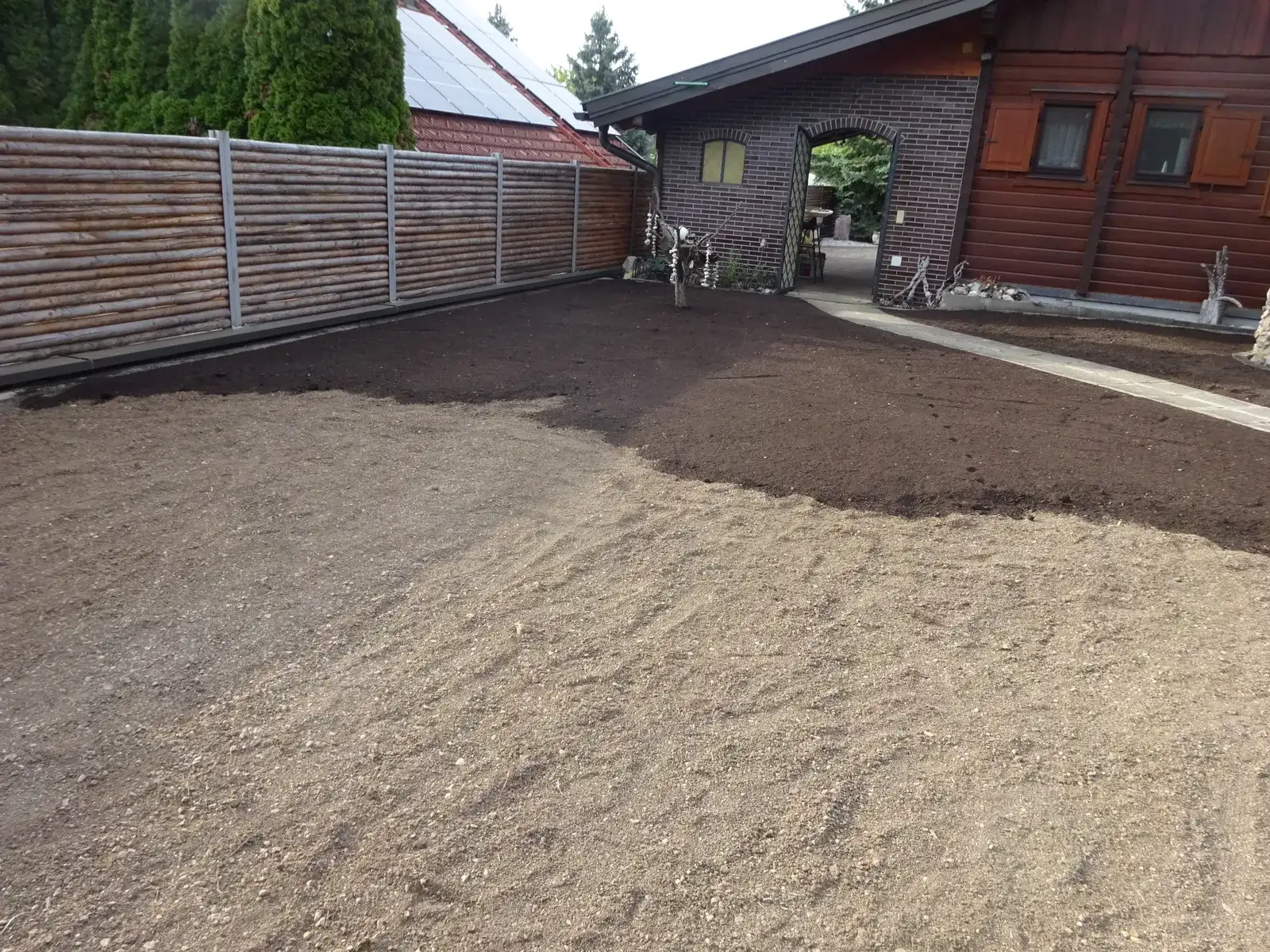 Frisch planierte, dunkle Erdfläche vor einem Haus mit Holzzaun