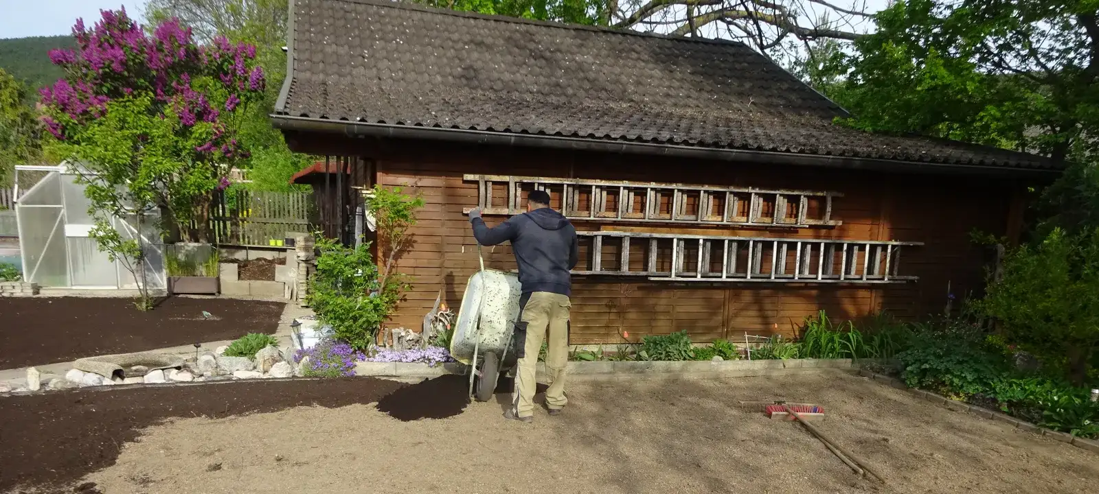 Mitarbeiter verteilt Komposterde auf einer eingeebneten Gartenfläche vor einer Holzhütte