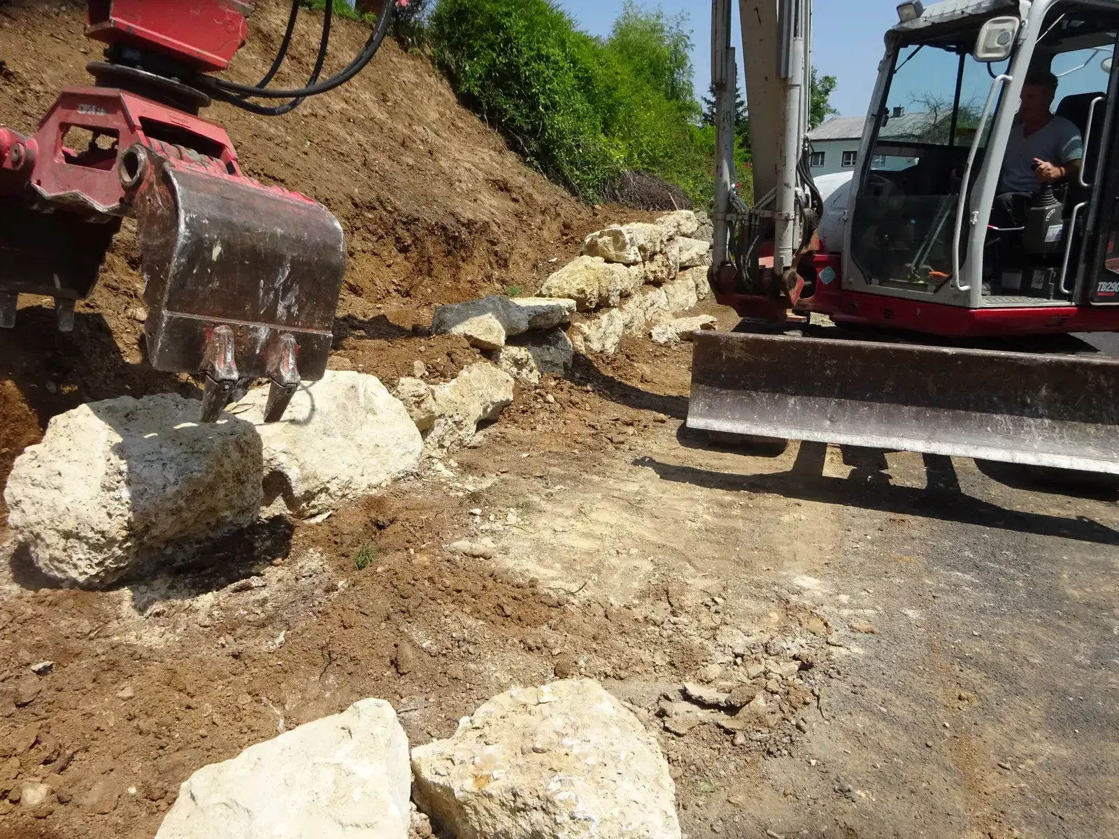 Bagger mit Schaufel setzt große Natursteinblöcke an einem Erdhang