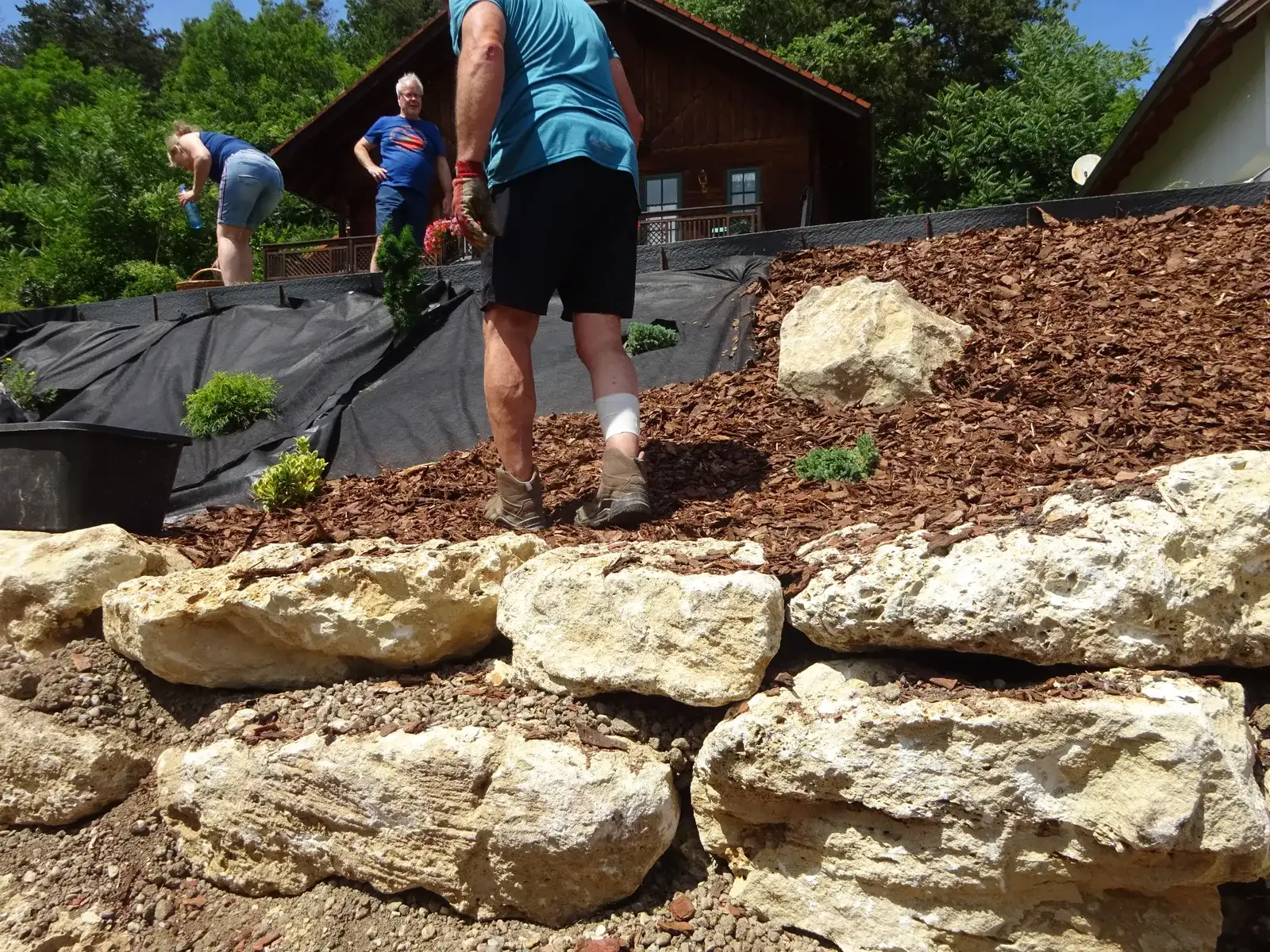 Große Natursteine einer Mauer, darüber wird eine mit Vlies und Rindenmulch abgedeckte Fläche bepflanzt