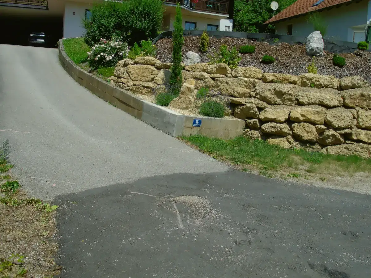 Natursteinmauer mit Bepflanzung entlang einer Hauszufahrt