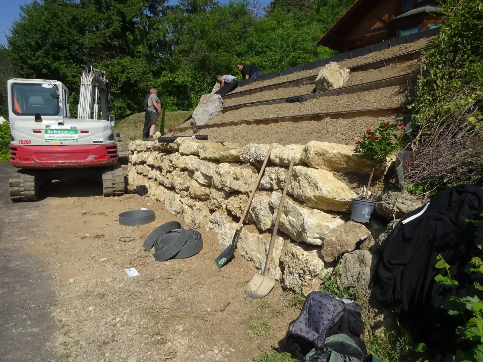 Bagger an einem Hang, an dem Natursteinmauern Terrassen abstufen