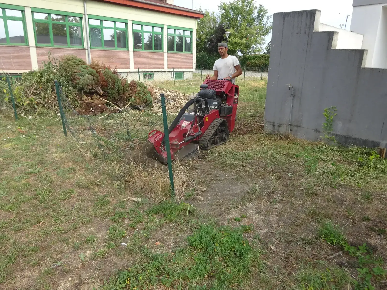 Mitarbeiter mit Stubbenfräse rodet eine Fläche neben einem Gebäude