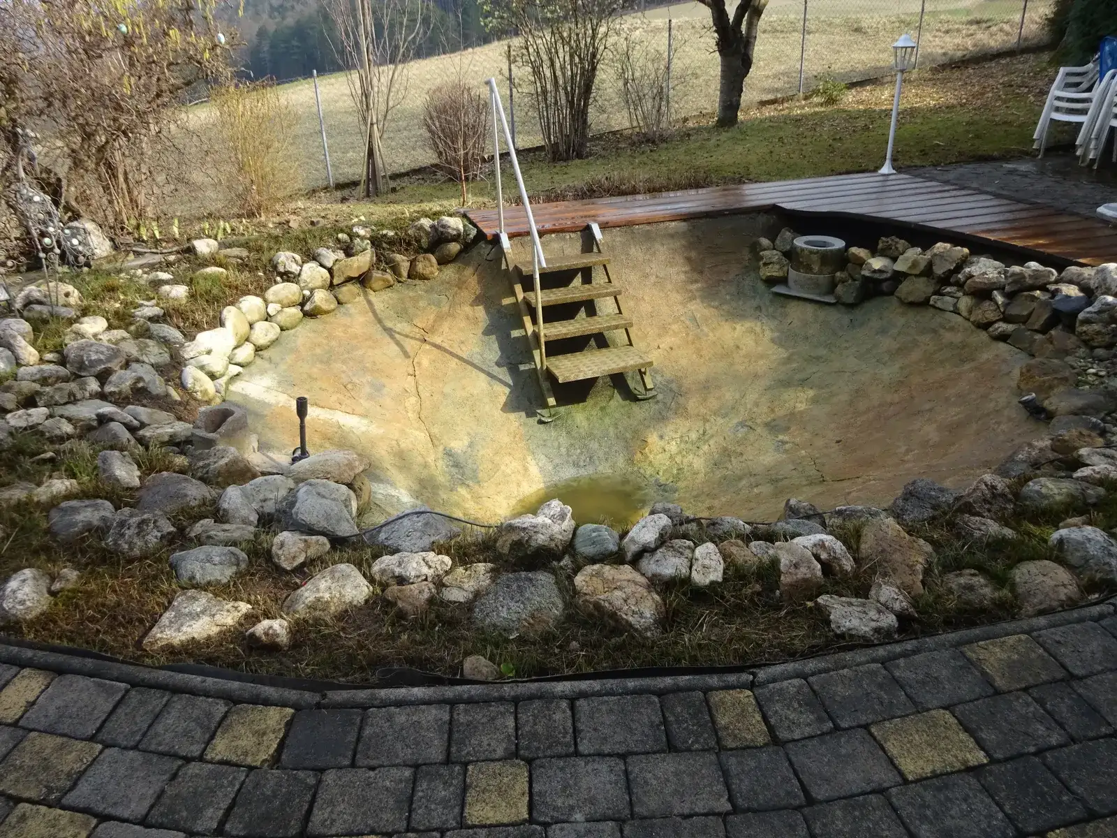 Abgelassenes, gereinigtes Teichbecken mit Holzstiege, umrandet von Natursteinen und einem Holzsteg